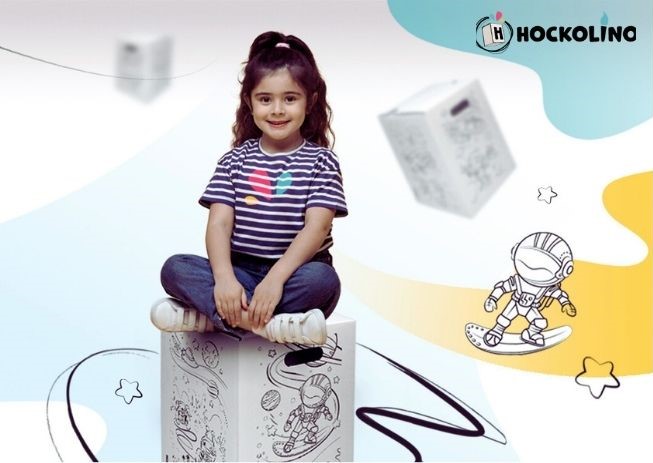 Lachendes Kind sitzt im Schneidersitz auf einem Hockolino mit Weltraum-Motiven, umgeben von schwebenden Zeichnungen.